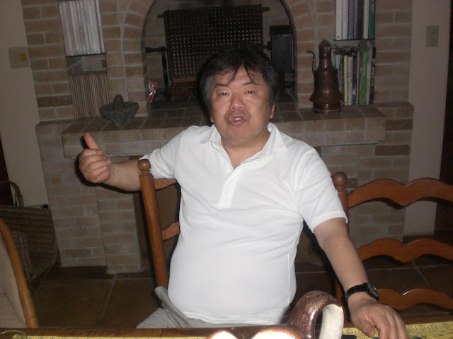 Masaki Iizuka at a dinner table at home, giving a thumbs up to camera