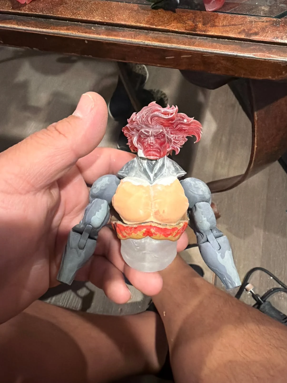 Part-built figure held in one hand, showing a red translucent 3D printed Lion-O head on a torso with unpainted grey arms
