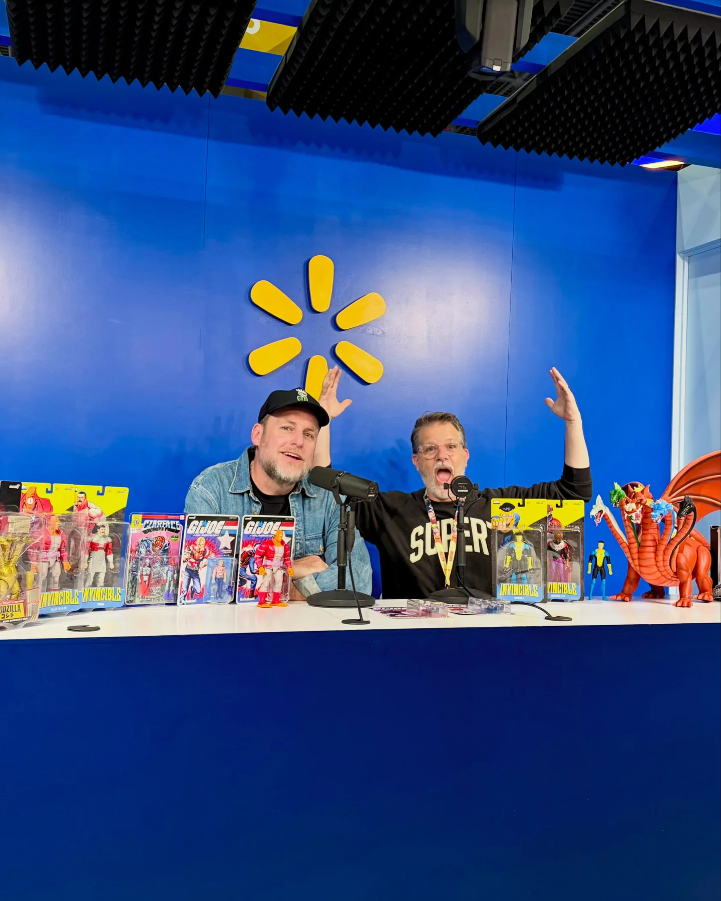 A many-headed orange dragon figure at the end of the table in the Walmart Live studio, beside Brian Flynn and Esoteric with their arms raised