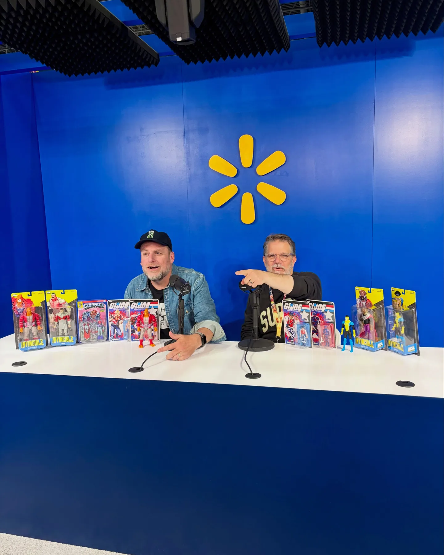Super7 founder Brian Flynn and Esoteric of CZARFACE at a table in the Walmart Live studio at NYCC, with Invincible, CZARFACE and G.I. Joe ReAction figures lined up in front of them
