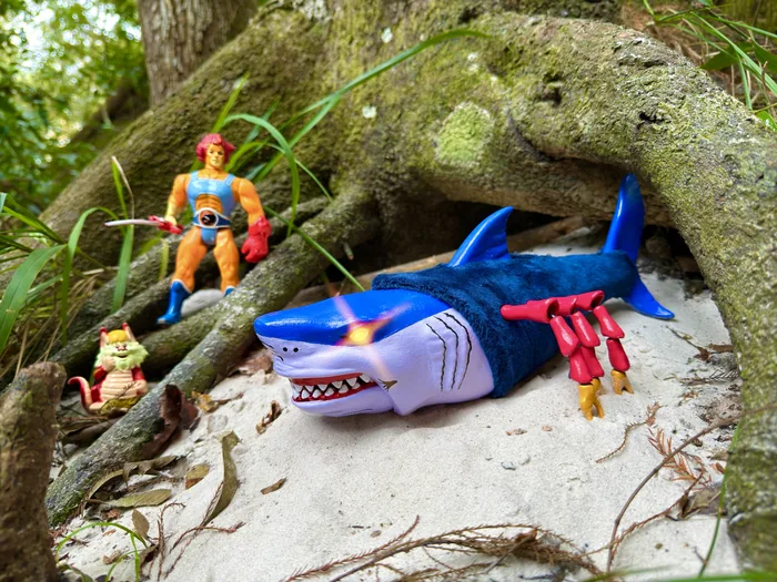 The custom Black Widow Shark beached on sand under a mossy root with vintage LJN Lion-O and Snarf figures behind